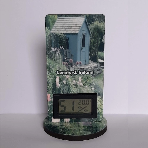 Personalised digital thermometer showing temperature and humidity with stand, featuring scenery with flowers a shed and text Longford Ireland